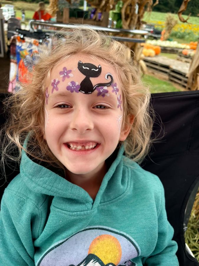 Girl with a black cat and purple flower forehead design at a fall pumpkin patch, In His Image face painting, serving Pigeon Forge TN