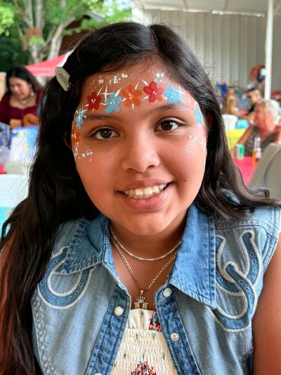 Girl with a colorful flower crown forehead design at an outdoor party, face painting by In His Image, Morristown TN
